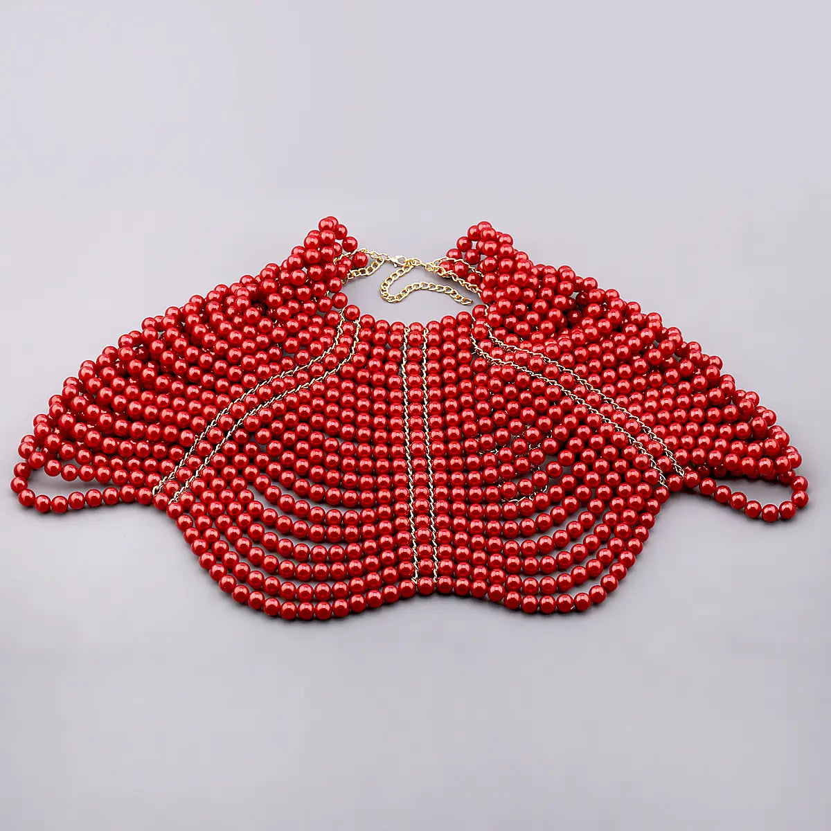 Collier de mode en chaîne corporelle de perles comportant un petit mantelet (capellet) en perles rouges, avec un décor de chaîne dorée.