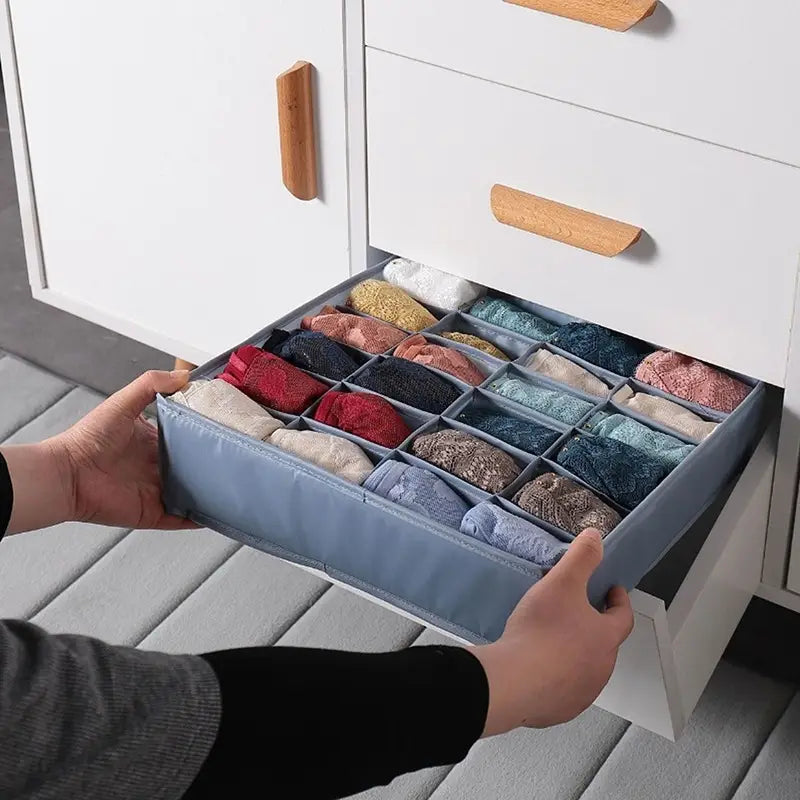 Organizador de cajón de tela azul con múltiples compartimentos para guardar lencería doblada y almacenar ropa interior y calcetines en un cajón de armario.