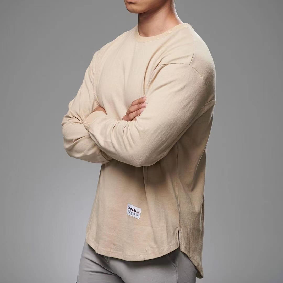 Beige men long sleeve cotton t shirt with a crewneck, subtle side slit, and small white label at the bottom hem.