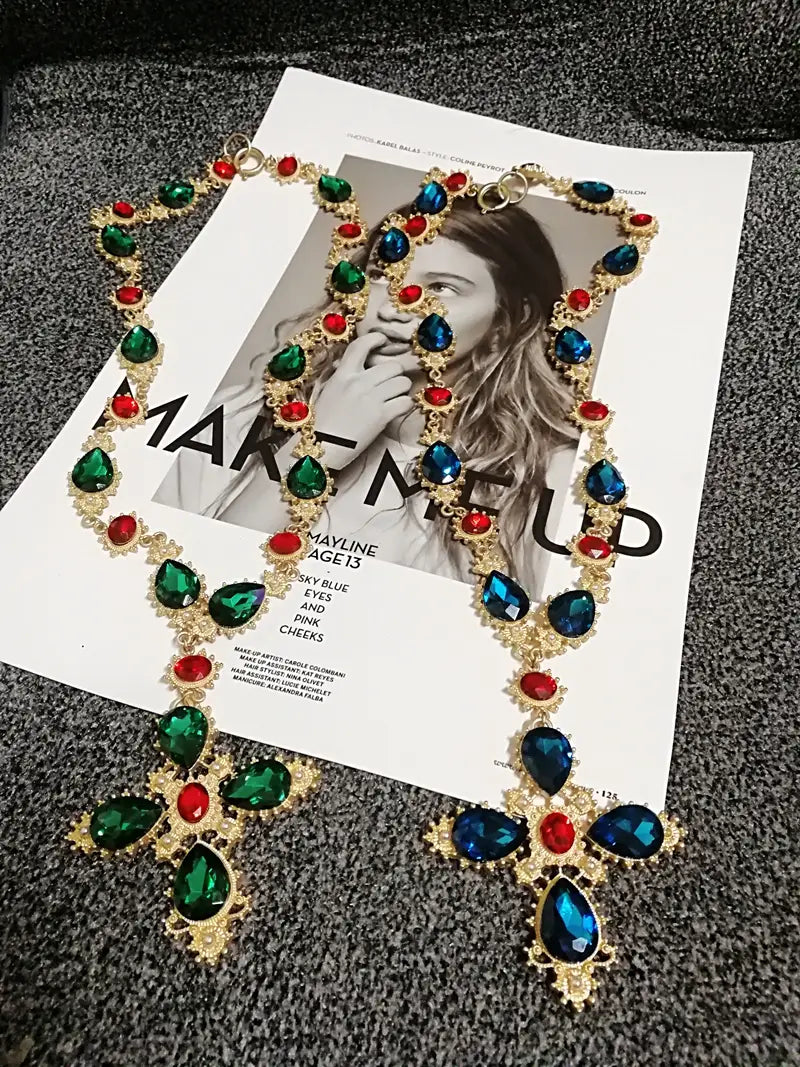 Collier ras du cou à déclaration en cristal à finition dorée, d’un éclat glamour, présentant un grand motif de cristaux facettés vert émeraude et bleu profond en forme de larme, ainsi que de pierres rouges plus petites, idéal pour des bijoux de soirée.