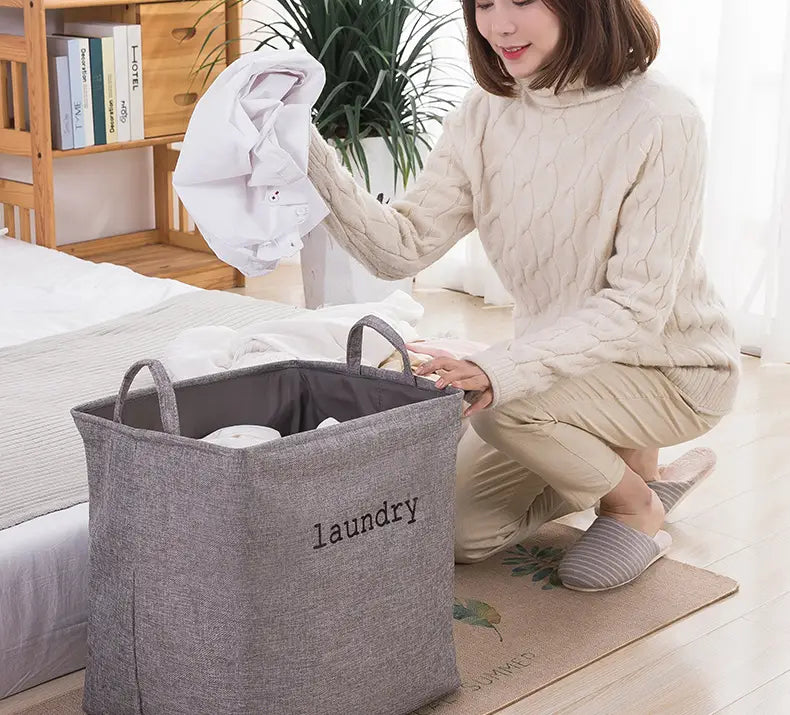 gray fabric laundry basket with black embroidered laundry text and sturdy handles designed as a foldable storage basket for organizing laundry and household items