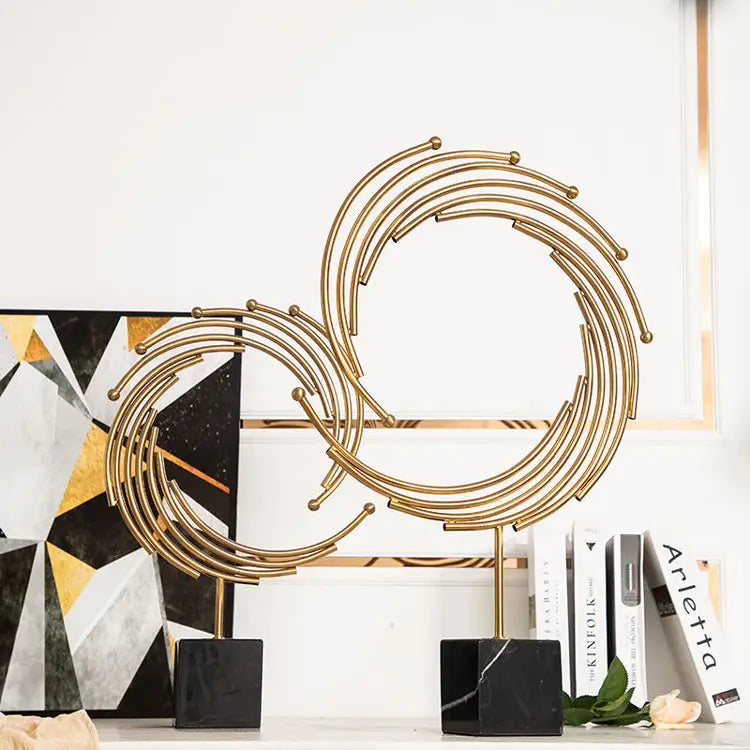 Gold metal abstract sculpture featuring interlocking circular rings and small spherical accents in gold tone with a black marble base designed as office desk decor.