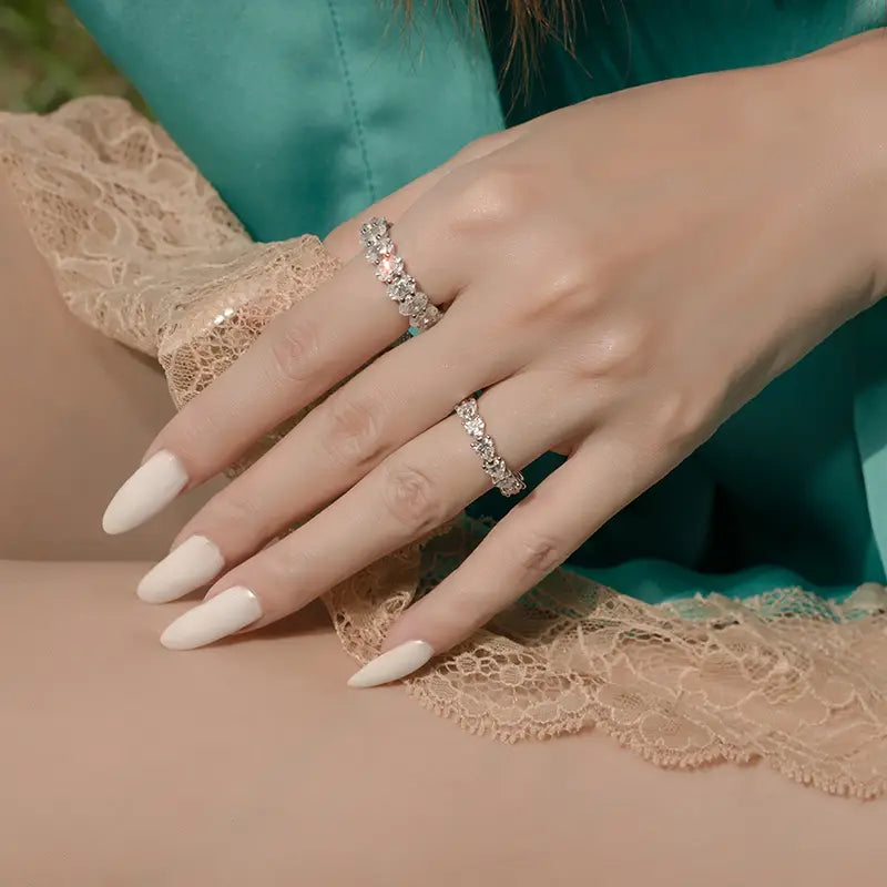 Une paire de deux élégantes bagues d’éternité cœur en argent sterling à tonalité argentée, avec des motifs complexes sertis de diamants, portées aux doigts.