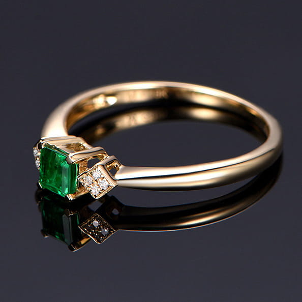 Ein Verlobungsring aus 18k Gold mit Smaragd und Diamanten: mit einem strahlenden smaragdschliffartigen, grünen Edelstein, eingesetzt in einem eleganten Goldband, das beidseitig mit funkelnden Diamanten akzentuiert ist.