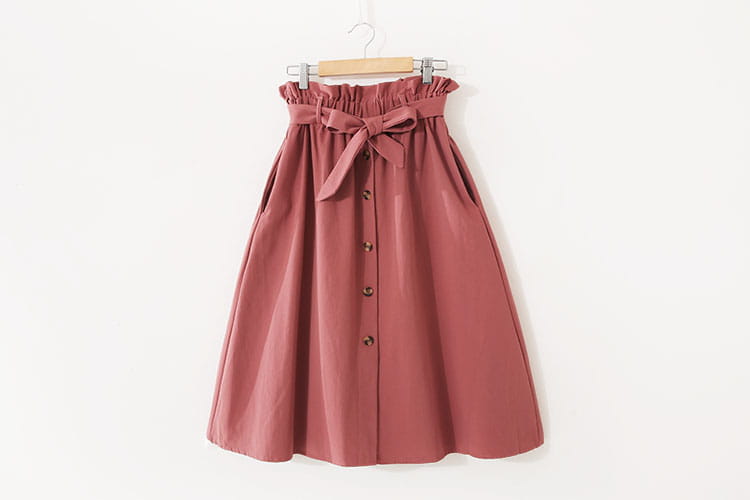 Jupe midi en coton rose tendre, à taille haute, ceinture froncée et nœud en tissu assorti, adaptée à une tenue décontractée.