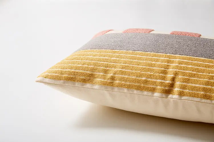 ein gemütlicher bestickter geometrischer Kissenbezug in den Größen 45x45 cm und 30x50 cm mit einer strukturierten grauen oberen Lage und horizontalen Senf-Gelb-Streifen sowie weichen Rosé-Farbdetails entlang der oberen Kante.