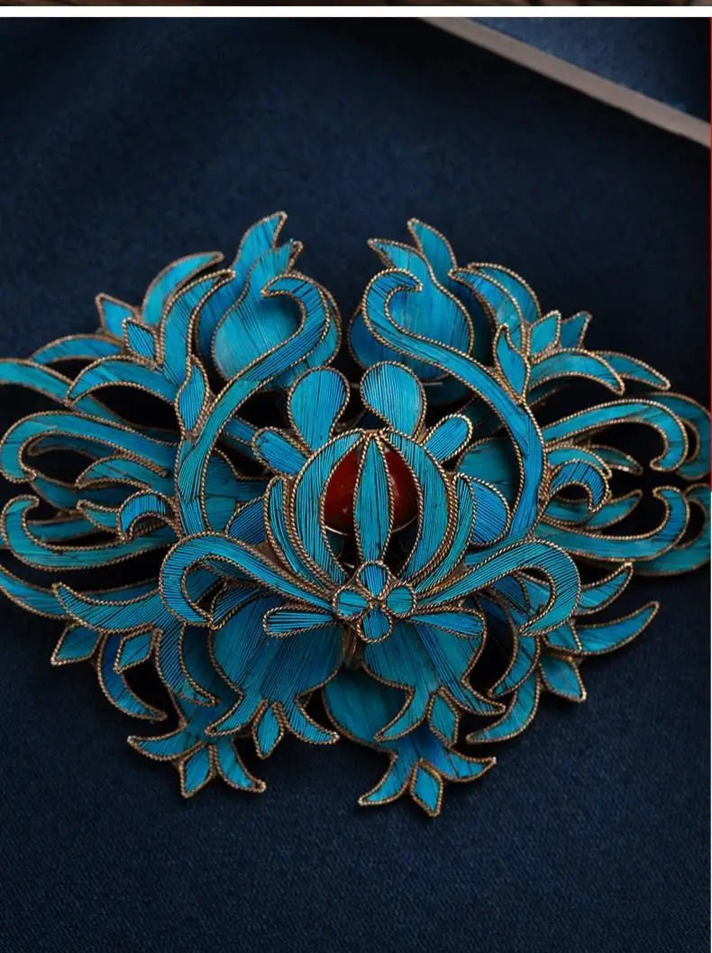 A vibrant turquoise enamel floral hair clip with gold-toned metal outlines and a central red gemstone accent from the filigree brooch turquoise floral palace jewelry collection.