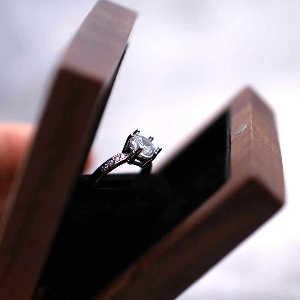 Ein funkelnder Diamant-Verlobungsring mit schlanker Silberfassung und kleinen Akzentsteinen, elegant präsentiert in einer geöffneten personalisierten Schmuckring-Schachtel aus Walnussholz zur Hochzeit.
