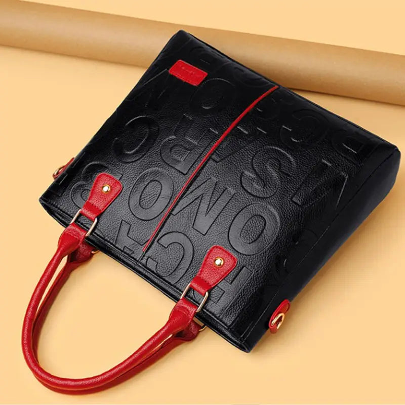 Black crossbody handbag style1 style2 made of black pu leather with embossed lettering and red handles trim and hardware in satchel style.