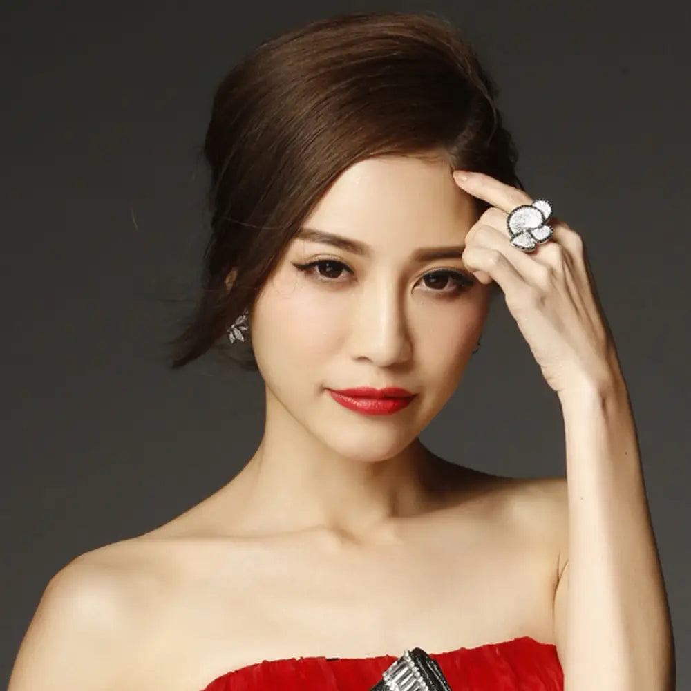A woman wearing a red strapless dress holds up a black and white crystal statement flower ring featuring an ornate silver design with multiple sparkling stones.