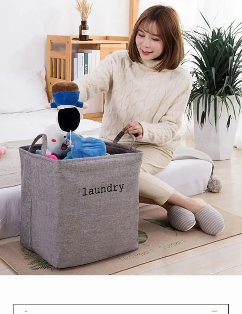 Gray fabric foldable laundry basket with laundry embroidered in black letters and two handles designed as a storage basket for organizing clothes.