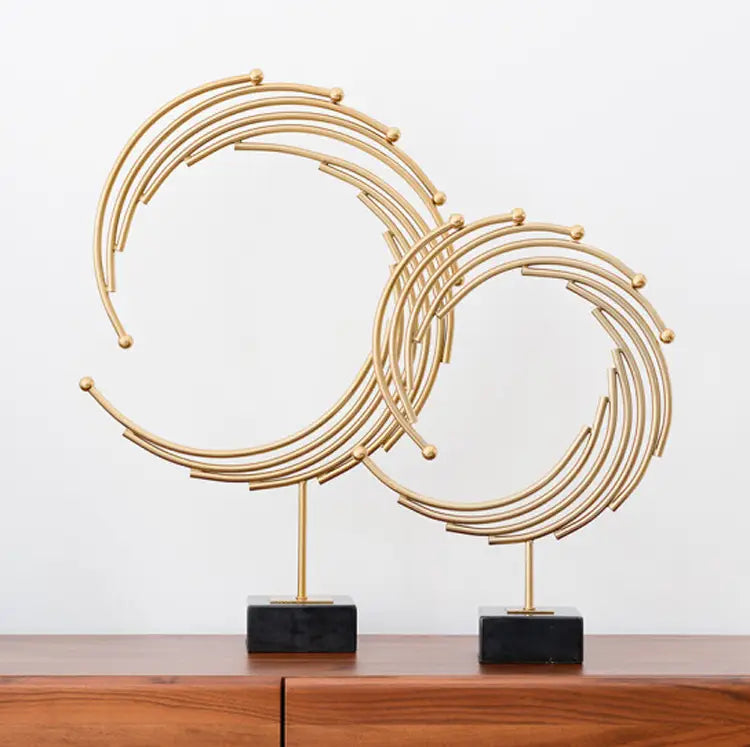Gold metal abstract sculpture featuring interlocking circular rings and small spherical accents mounted on black marble bases designed for office desk decor.