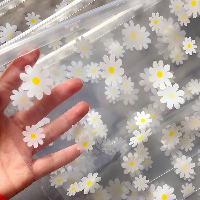 Blumige, durchsichtige Reisekosmetiktasche aus durchsichtigem Kunststoff, verziert mit weißen Gänseblümchen mit gelben Zentren.