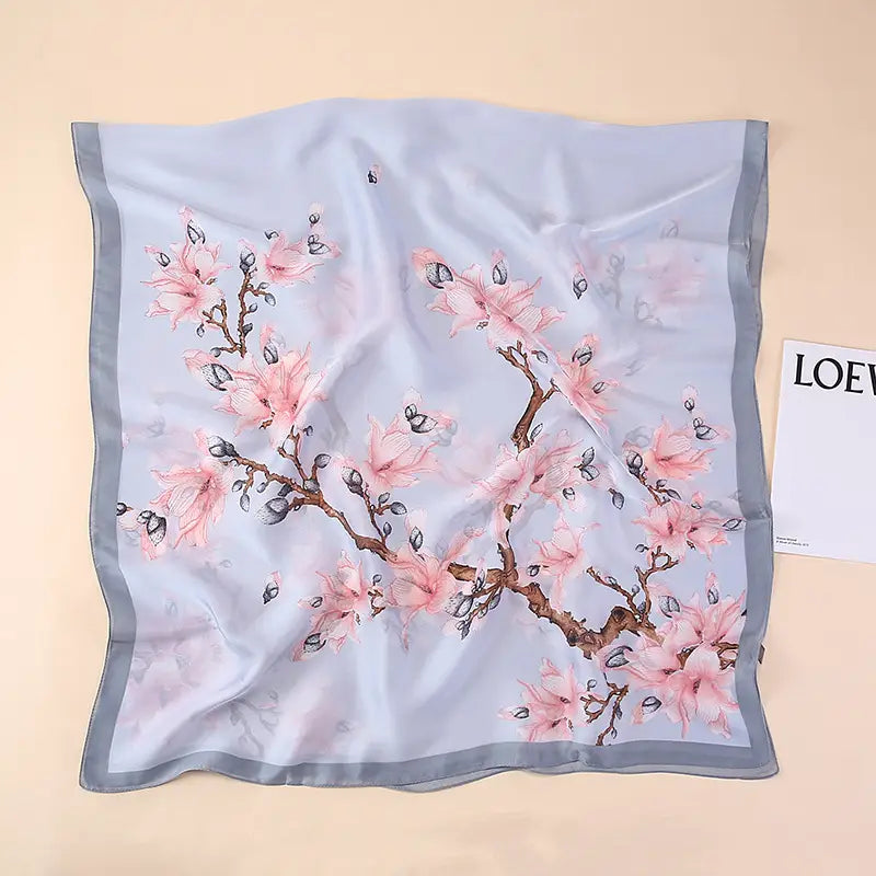 Un foulard en soie bleu clair délicat, avec un motif de cerisiers en fleurs rose pâle, des branches brunes et des boutons noirs, encadré par une bordure gris subtil, issu de la collection des amandiers en fleurs de Van Gogh.