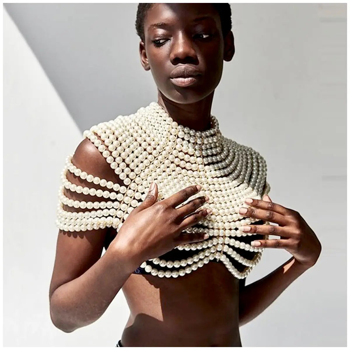 Une pièce d’épaule sculpturale blanc cassé, ornée de perles, avec des rangées superposées de perles formant un design structuré à col haut, dans le cadre d’un collier de mode en chaîne corporelle de perles.