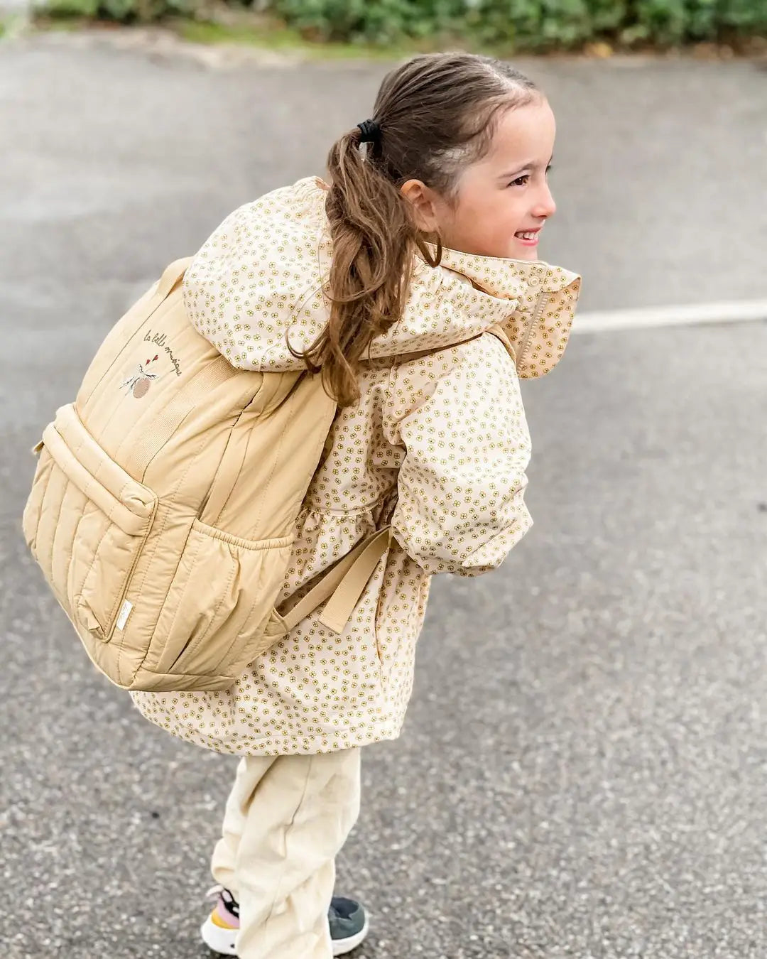 Beiger Kinder-gesteppten Rucksack aus wasserfestem Material mit kleiner floraler Stickerei auf der Vorderseite, geeignet für die Schule.