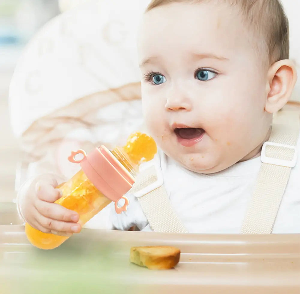 Orangefarbene Silikon-Babysqueeze-Feedingflasche mit rosa Silikondeckel und Griff, ausgelegt für einfaches Füttern und das Abgeben des Löffels.