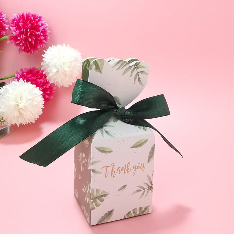 Eine zarte weiße Papier-Hochzeits-Gastgeschenkbox mit dezentem Grünblattmuster und „Danke“ in Roségold-Schrift, gebunden mit einem dunkelgrünen Satinband.