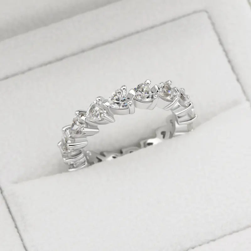Une bague d’éternité cœur en argent sterling, dotée d’une bande argentée élégante ornée d’une rangée continue de diamants ronds étincelants, sertis dans un motif de sertissage sécurisé à griffes.