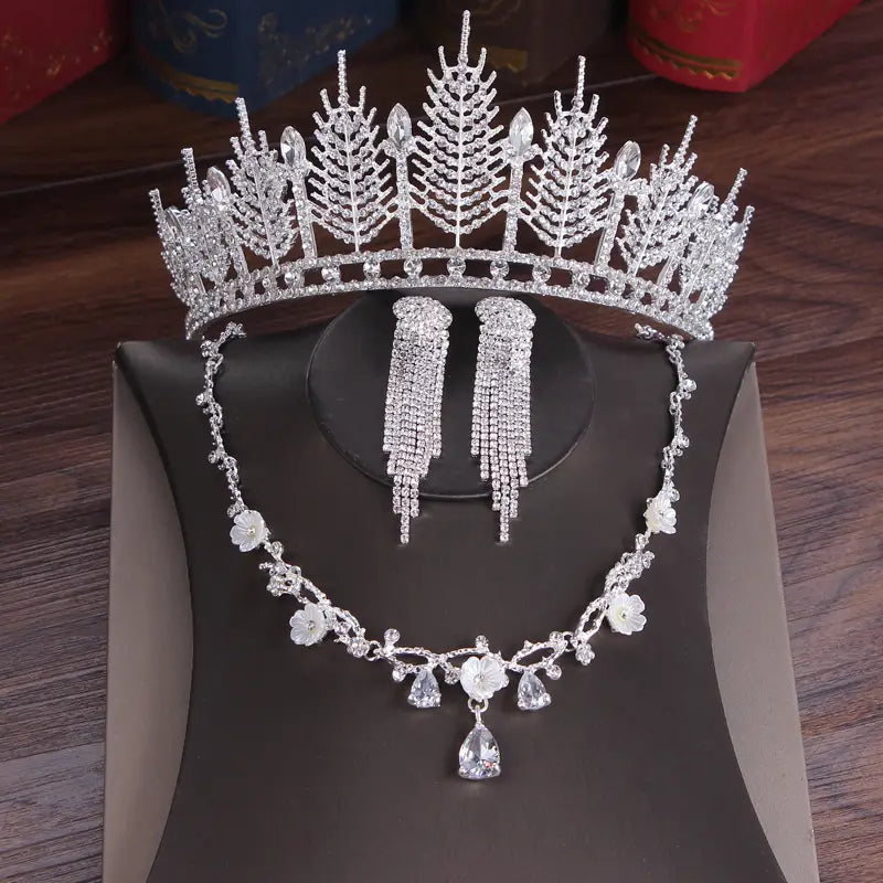 Silver crystal bridal tiara and wedding crown headpiece adorned with intricate leaf and crystal designs featuring a sparkling centerpiece and delicate dangling earrings.