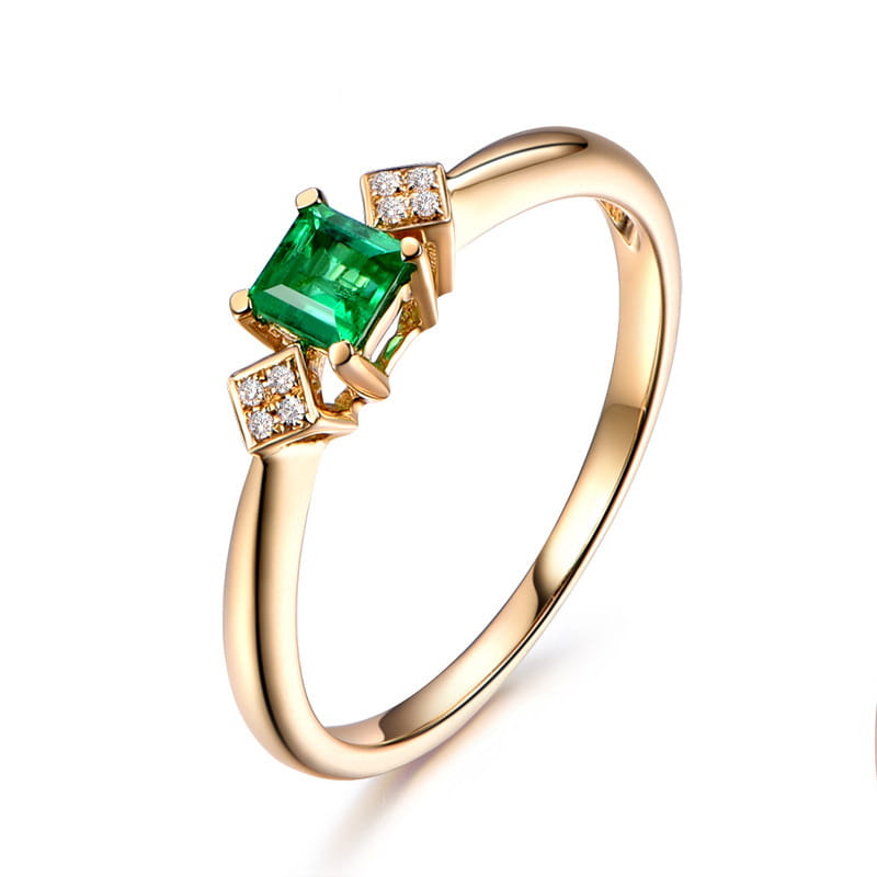 Ein Verlobungsring aus 18k Gold mit Smaragd und Diamanten: mit einem zentralen smaragdschliffartigen, grünen Edelstein, flankiert von zwei quadratischen Ansammlungen kleiner Diamanten.