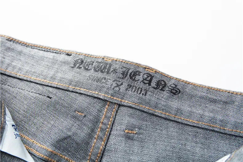 Jeans en denim stretch pour hommes, coupe regular fit, en gris, avec un délavage décoloré et des coutures marron, présentant la nouvelle étiquette de marque de jeans brodée en fil noir au dos.