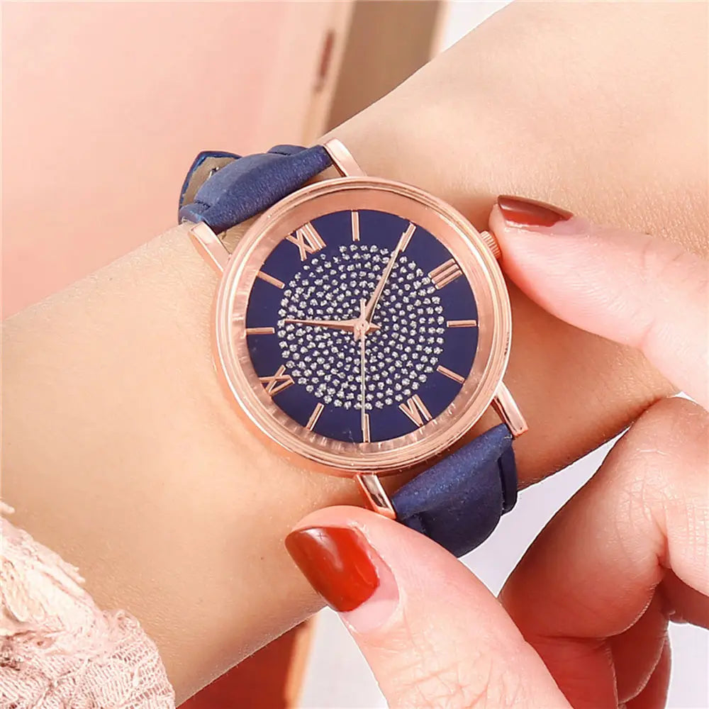 A rose gold crystal quartz women watch with a navy blue leather strap and a roman numeral dial adorned with sparkling crystals.