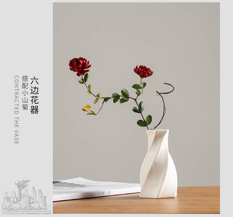 A modern white ceramic vase with a sleek twisted design holds two vibrant red chrysanthemums for floral decor.