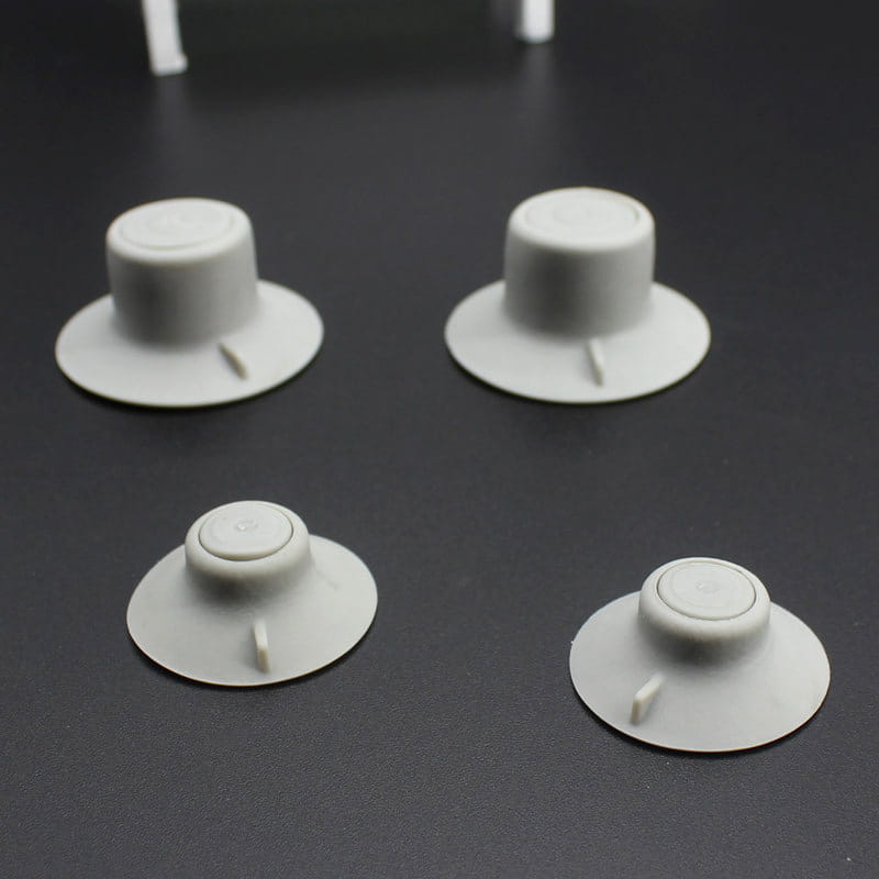 quatre patins de réduction de la chaleur sous forme de boutons en plastique blanc cassé pour pieds de refroidissement d’ordinateur portable, avec bases circulaires et petites languettes en saillie.