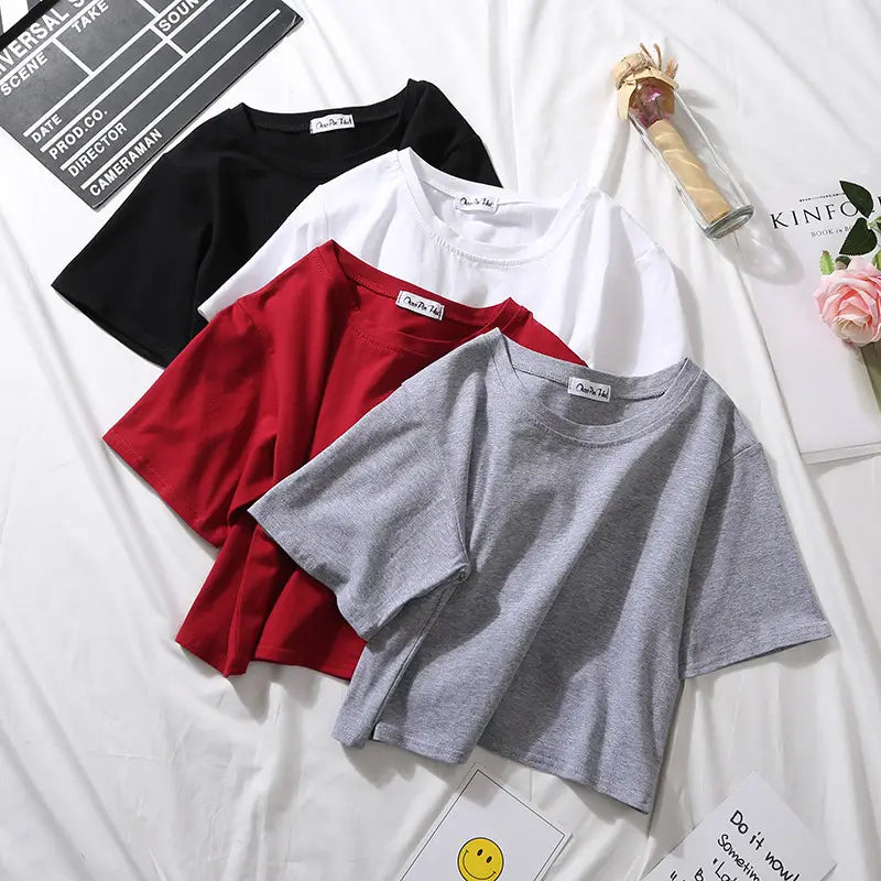 Four cropped short sleeve cotton t-shirts in black white red and heather gray neatly arranged on a white surface for casual wear.