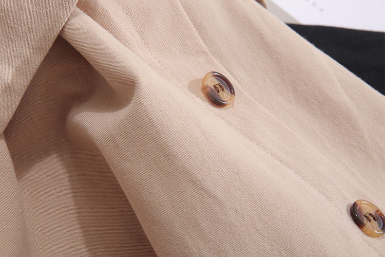 Manteau beige de type trench avec boutons écaille assortis, porté avec une jupe midi en coton à taille haute, dans un style de robe décontractée en coupe ligne A.
