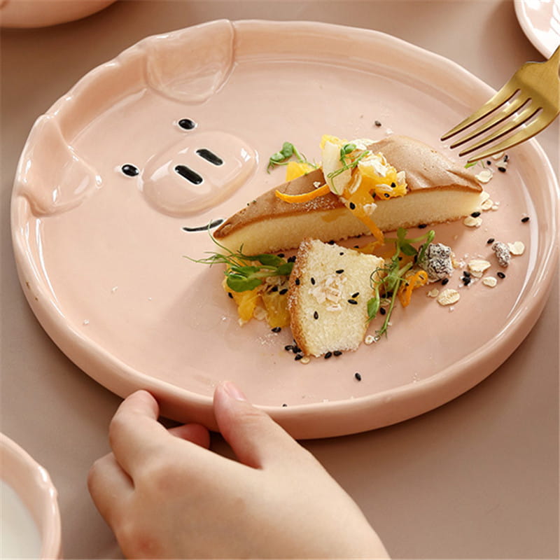 A pink ceramic plate shaped like a pig with black eyes and snout details from the cute pig ceramic dinnerware set.