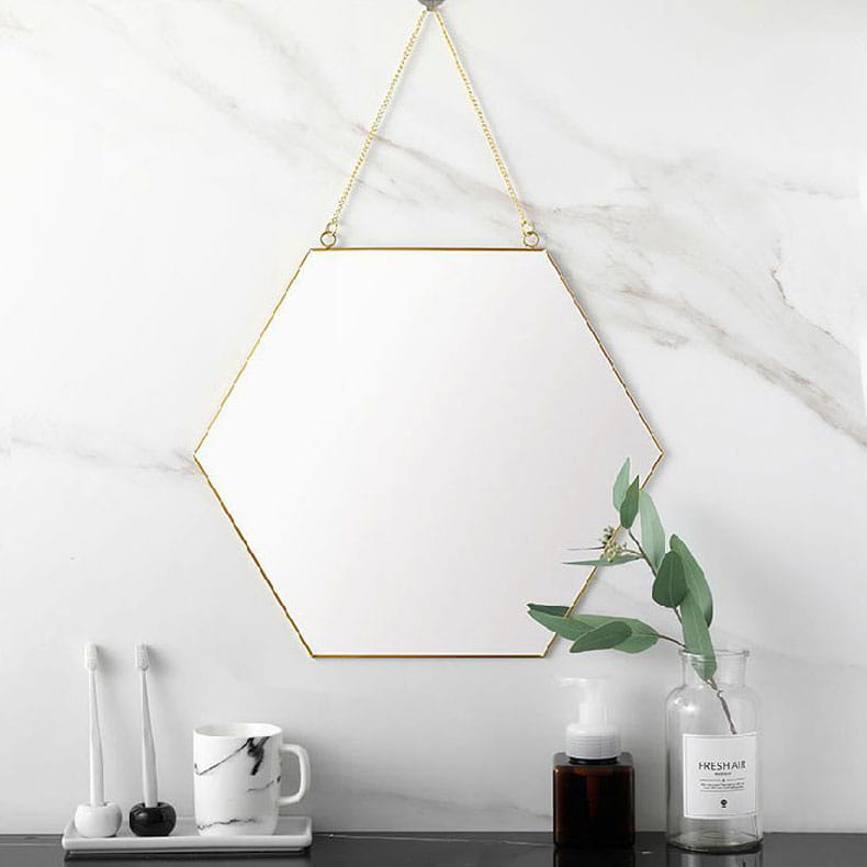 A gold hexagonal wall hanging mirror with a thin metal frame and a hanging chain.