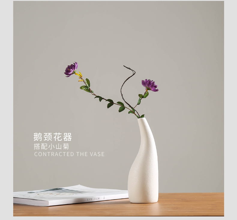 A sleek modern white ceramic vase with a slender neck and curved body holds two purple flowers for floral decor.