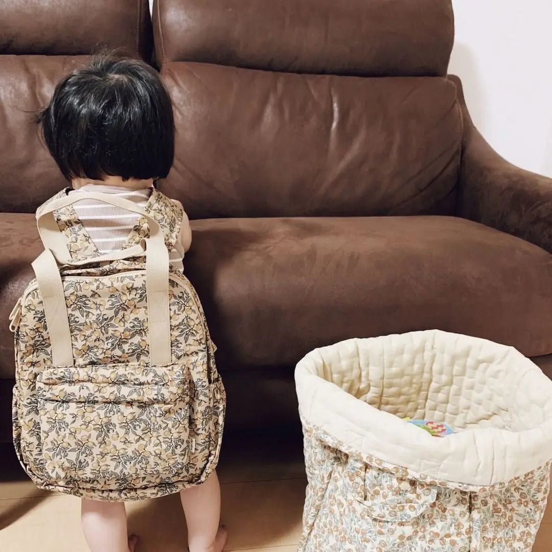 Ein Kind mit einem beigen Kinder-gesteppten Rucksack mit floralem Muster, besticktem Design, passenden Trägern und mehreren Taschen, konzipiert als wasserfester Schulrucksack.