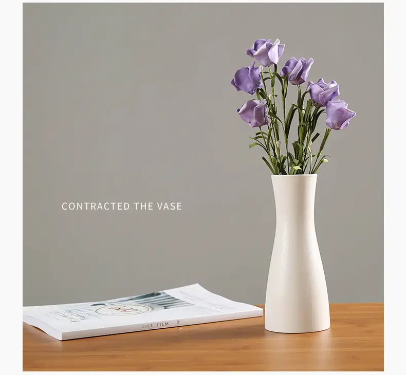 A modern white ceramic vase with a slender tapered design holds delicate purple flowers for floral decor.