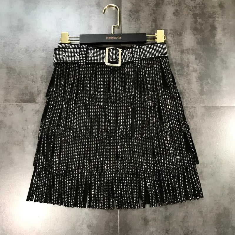 Mini-jupe noire à franges avec strass scintillants et ceinture assortie à rivets, présentant une boucle à tonalité argentée dans une coupe taille haute.