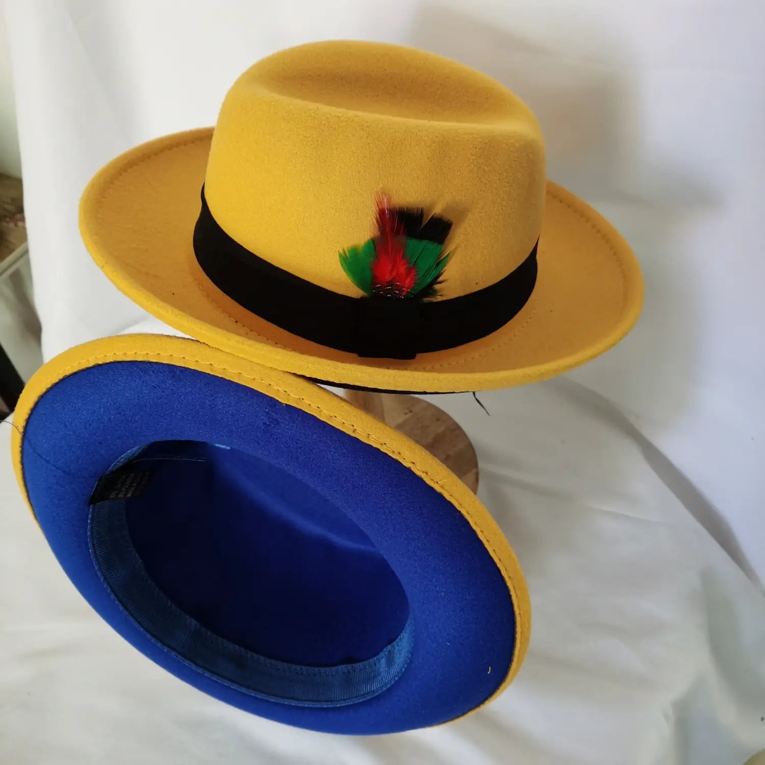 Unisex woolen felt fedora hat in yellow featuring a black band and red green feather accent.