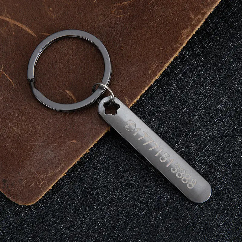 A sleek matte black metal custom phone number keychain with a rectangular laser engraved tag featuring numbers and a star-shaped cutout at the top.