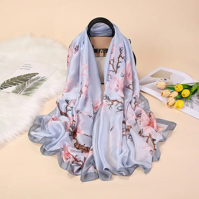 Un châle foulard en soie bleu clair doux, présentant un motif floral délicat avec des fleurs roses et des branches brunes, inspiré par les amandiers en fleurs de Van Gogh