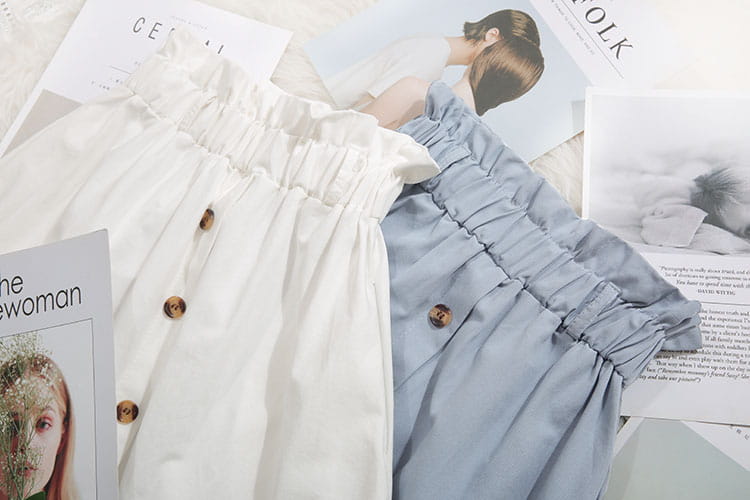 Deux jupes midi en coton à taille haute en écru, avec des boutons en bois et un tissu de style denim bleu clair, idéales pour une tenue décontractée.