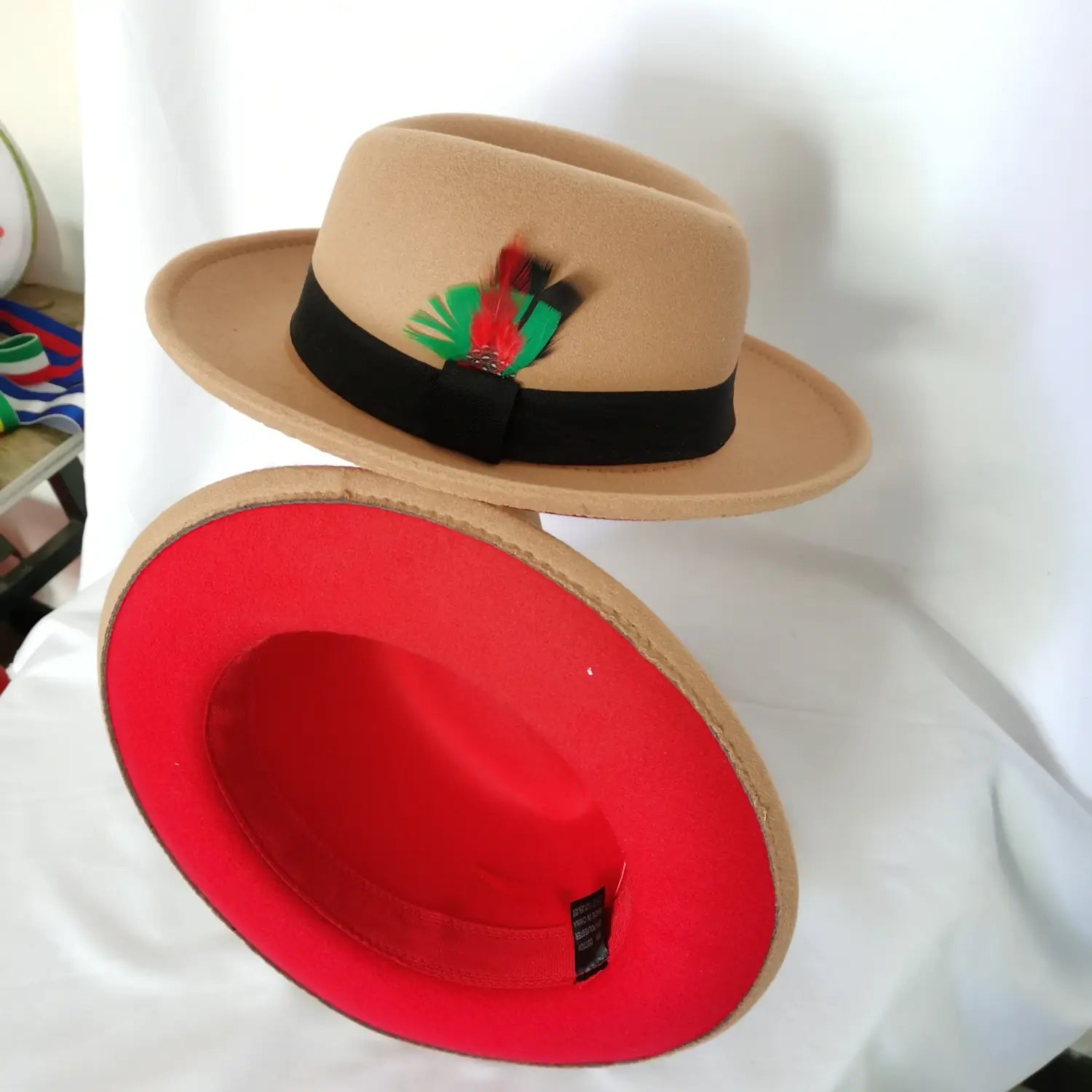 Beige unisex woolen felt fedora hat with black ribbon band and colorful feather accent featuring vibrant red interior lining.