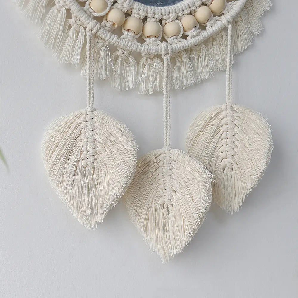 Cream-colored macrame wall mirror with woven leaf-shaped tassels and wooden beads for living room home decor.
