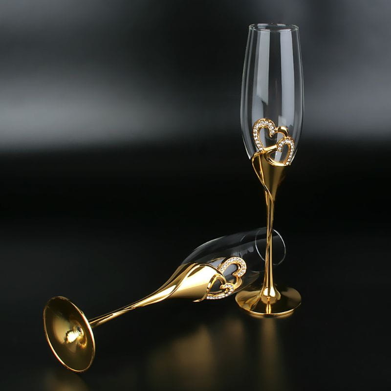 Elegant gold-toned wedding champagne flutes featuring intertwined heart-shaped embellishments encrusted with sparkling rhinestones for toasting.