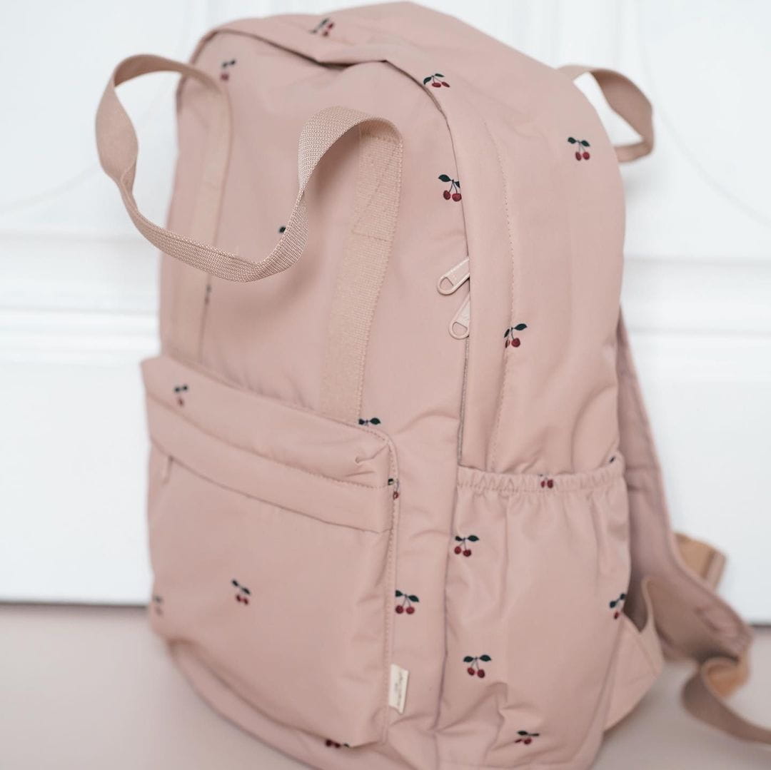 Ein weicher blush pinkfarbener gesteppten, bestickten Kinder-Rucksack mit dezentem Kirschenmuster und Stoffträgern, entworfen für den Schulgebrauch.
