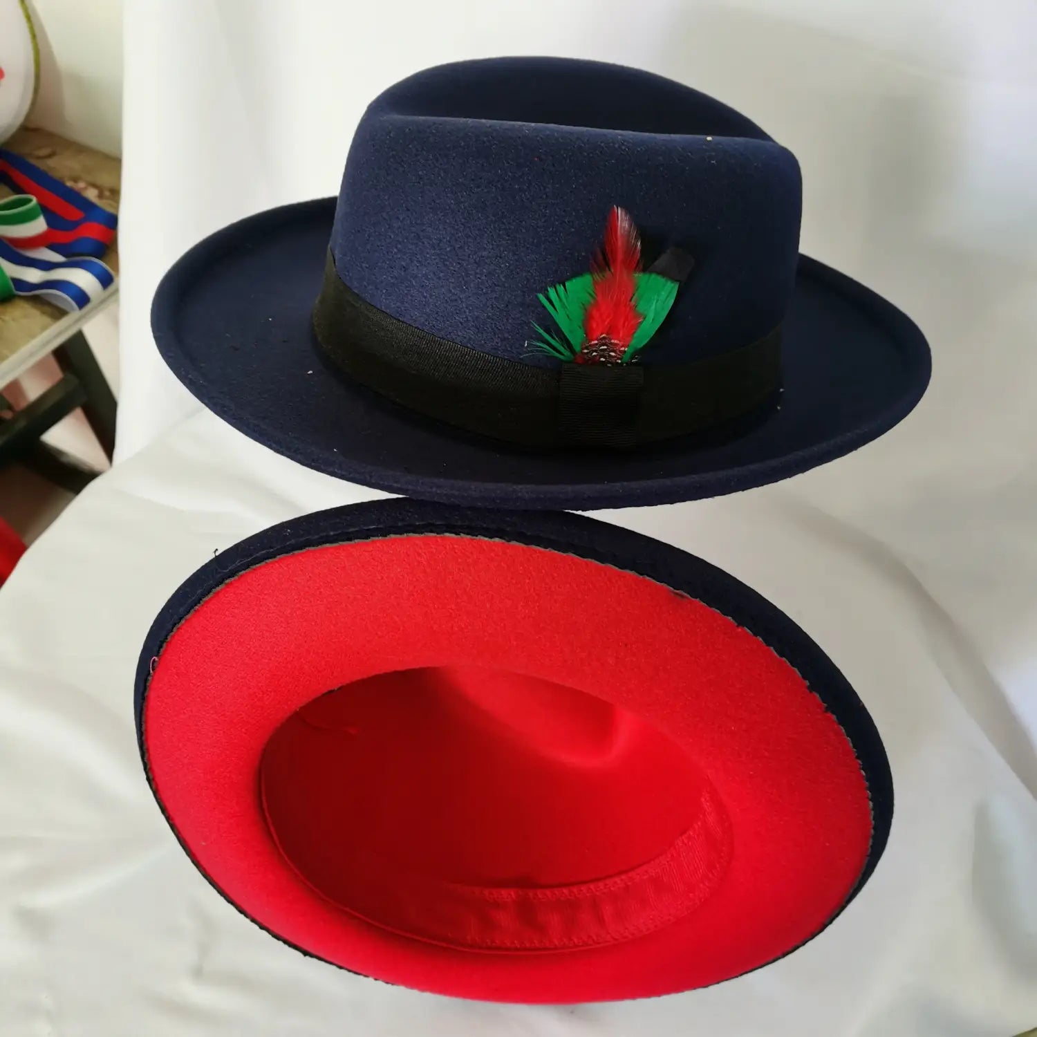 Navy blue unisex woolen felt fedora hat with black ribbon band and red feather accent featuring vibrant red interior lining.