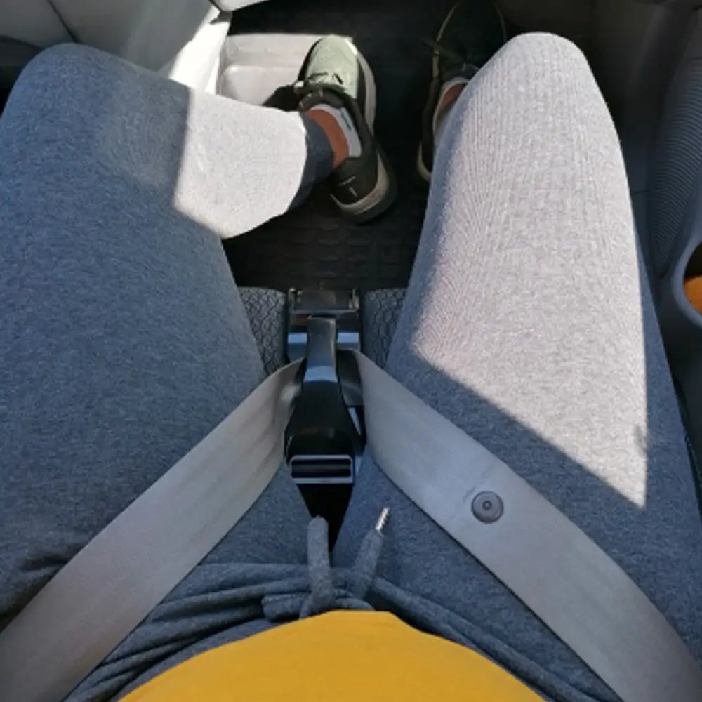 Grauer Stoff-Versteller des Autogurts für Schwangere mit schwarzer Kunststoffschnalle und silbernem Metallverschluss, quer über dem Schoß einer Person in einem Auto getragen, für Schwangere.