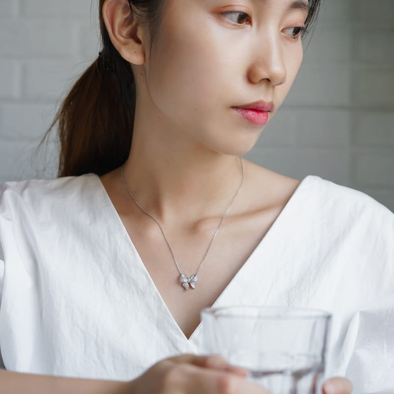 A delicate silver bowknot zircon necklace featuring a sparkling four-leaf clover pendant and matching earrings set.