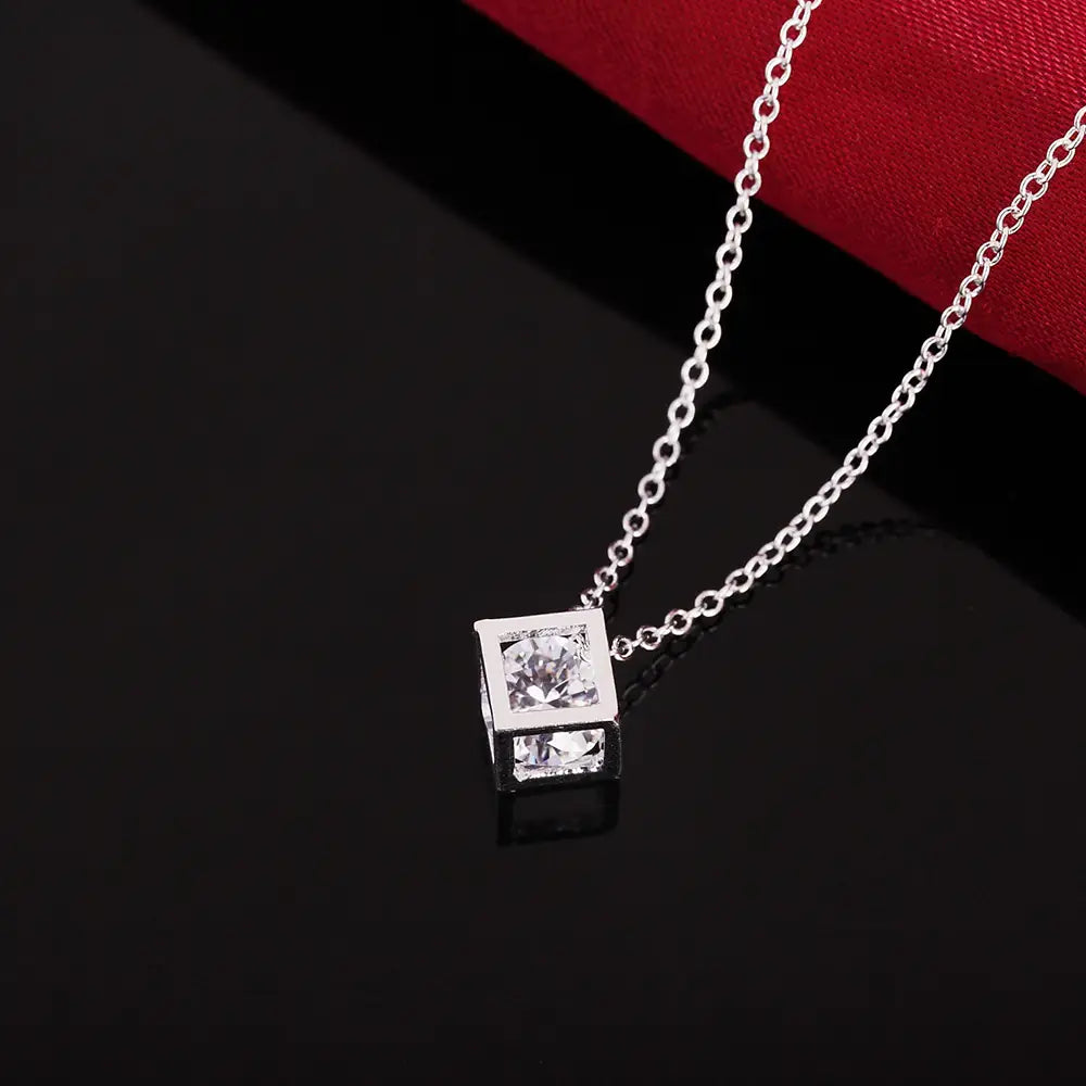Collier de pendentif en zirconium carré argenté, avec un collier en argent comportant un pendentif carré serti de deux pierres précieuses transparentes à facettes dans un cadre métallique élégant.