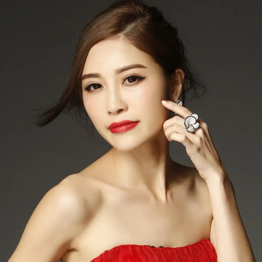 A woman wearing a vibrant red strapless dress with ruched detailing showcasing a black and white crystal statement flower ring.